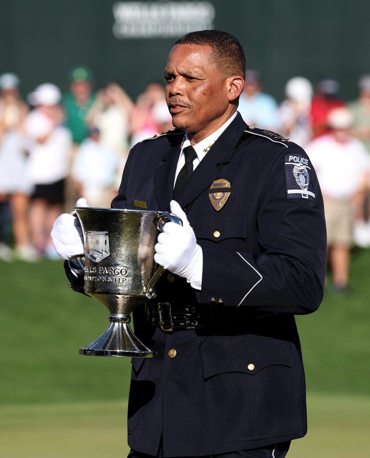 CMPD Chief Johnny Jennings carries the Wells Fargo Championship trophy from the department’s helicopter at Quail Hollow Club in Charlotte, NC on Sunday, May 12, 2024. CMPD Chief Jennings carried the trophy to the 18th green during a ceremony honoring the four law enforcement officers who died on Monday, April 29, 2024. Golfer Rory McIlroy won the championship at -17.
