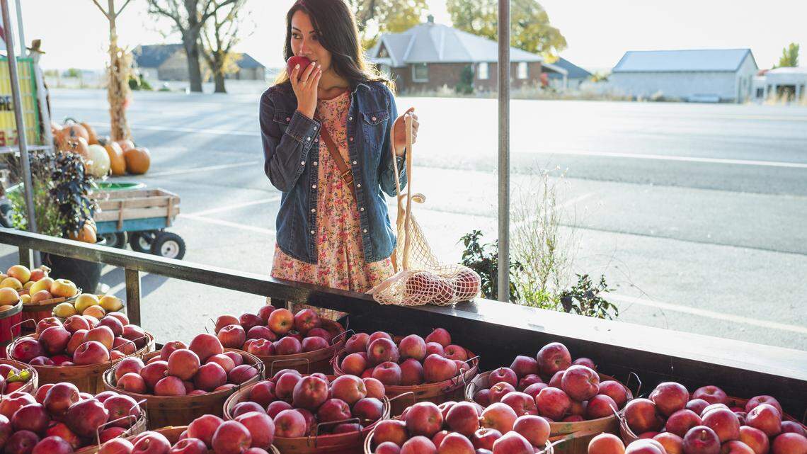 A woman picking out fresh local produce at a farm stand. 