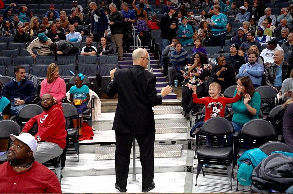 Jim Kobos engages with a young fan from his regular spot between sections 115 and 116 on the lower level of Spectrum Center during a recent Charlotte Hornets game.