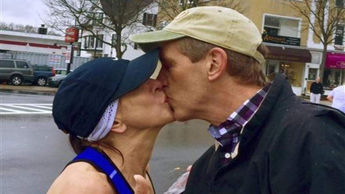 In this April 20, 2015 photo provided by Paige Tatge, her mother, Barbara Tatge, left, kisses an unknown spectator in Wellesley, Mass., as she ran in the Boston Marathon. It's a tradition for male runners to kiss the women attending Wellesley College as they line the marathon route. Barbara made good on a dare by her daughter, Paige, that she kiss a man as she ran along the route. Now they would like to know who she actually kissed.