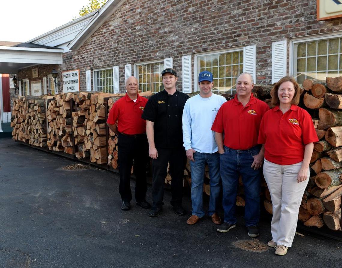 Family members Lloyd Bessinger, Chris Bennett, Paul Bessinger Jr., Paul Bessinger Sr. and Debbie Bennett stand in front of the hickory and oak logs used in the barbecue pits.