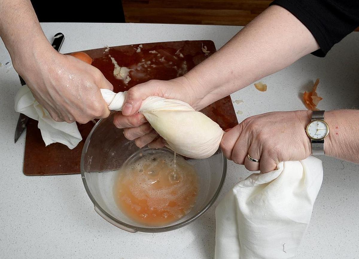 It takes two: Squeezing the water out of the grated potatoes is one of the tricks to better latkes. It helps to have two people to really twist and squeeze.