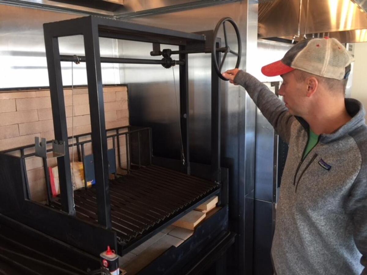 Chef/owner Trey Wilson calls his wood-cooking apparatus, with hooks, a pulley and ridged grill, “the main attraction.”