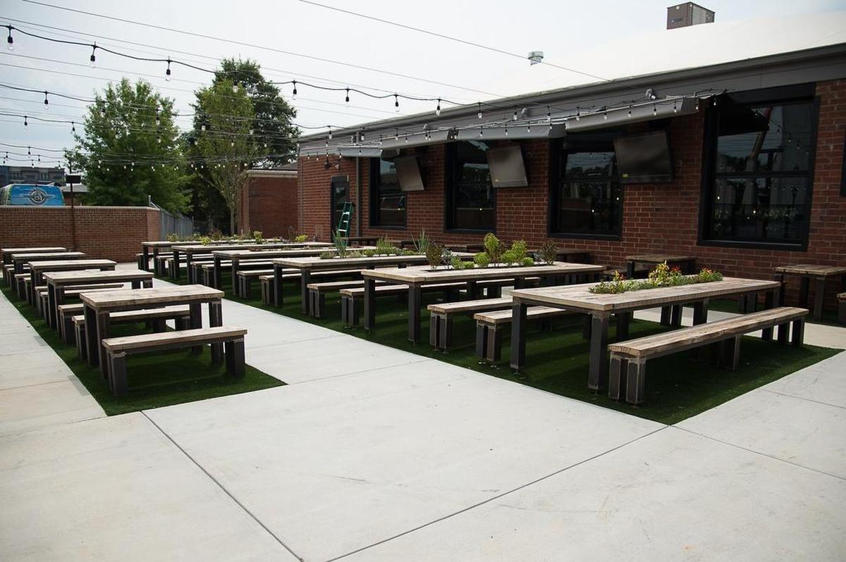 The outdoor space includes tables with inset herbs and plants and umbrella covers to keep the summer heat off.