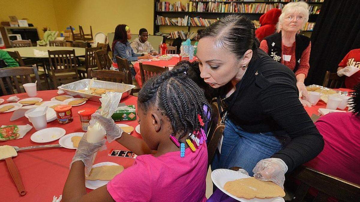 Volunteer Casonia Shortridge, with Aramark food service, assists kids with decorating holiday cookies at the Salvation Army Center of Hope in Chalotte Monday.The party for low-income children included a $10 gift certificate for them to spend on themselves.
