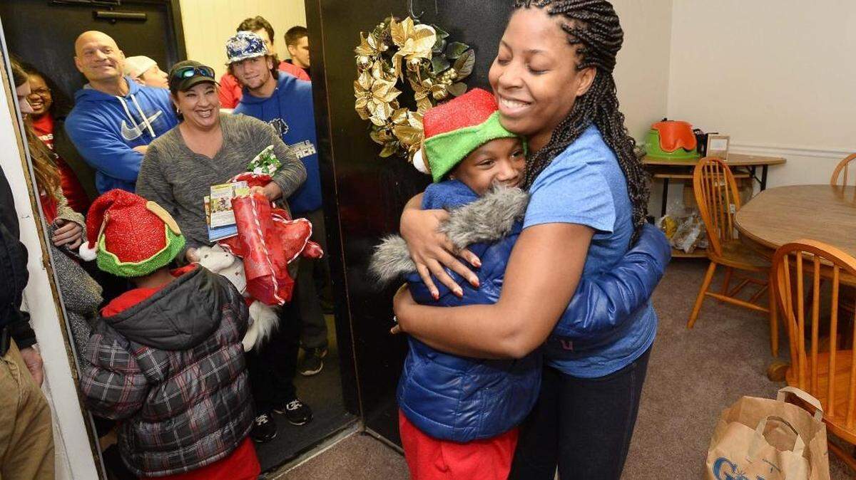 From left, volunteer Kelsey Brooks 9, receives a thank you hug from Crystal Fuller after Kelsey Brooks helped to deliver gifts for Crystal's family of four children at her apartment, during the CMPD Explorers Christmas Project, volunteers and explorer scouts watch from the hallway on Dec. 19,2015.