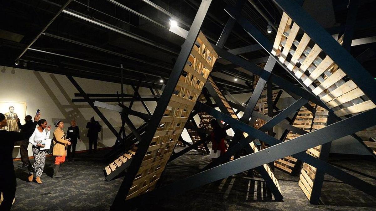People walk around and through the work Tunnel X by artist Serge Alain Nitegeka, in the exhibit Venturing Out of the Heart of Darkness, at the Gantt Center. In this work, the artist uses light, space and wood to encourage viewers to explore the psychological and physical space of their own minds and bodies.