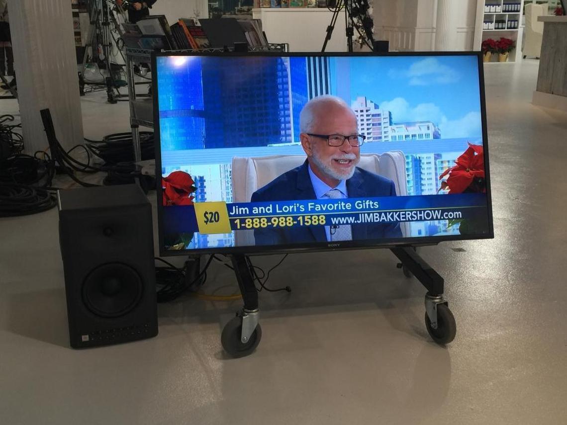 Jim Bakker shows up on a TV monitor in one of the studios where he tapes his daily hour-long TV talk show. His co-host is wife Lori. Products available for a specific donation amount are often advertised at the bottom of the screen during the show, which is broadcast and streamed from deep in the Ozark Mountains of Missouri.