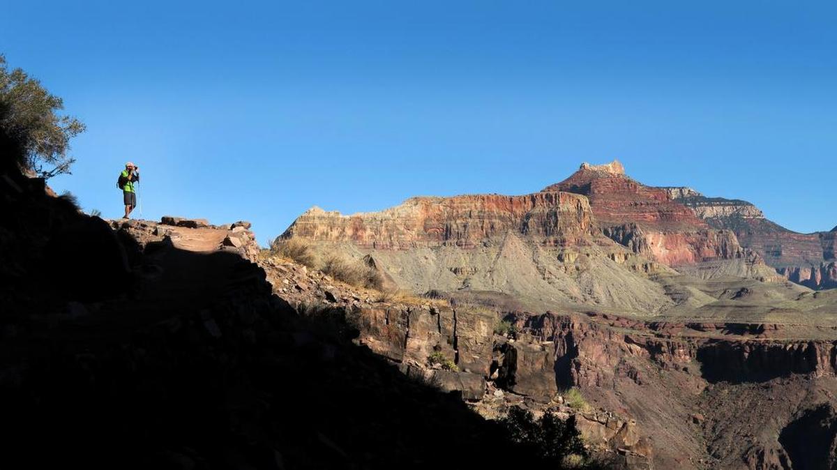 Two-thirds of the way down the South Kaibab Trail, a hiker stops to take a photograph of the Colorado River. Between the canyon's South Rim and the Colorado River, the trail passes through 30-some layers of rock, which cover 1.8 billion years of geologic time.