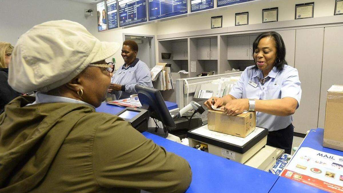 From left, customer Hazel Grier has a package - a Christmas present for her grandchildren in Texas - weighed and shipped by USPS sales service associate Wonga Watts at the USPS Plaza Station on East W.T. Harris Boulevard on Dec. 17, 2015.
