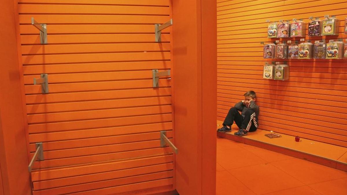 A child sits next to the empty toy displays at the Toys R Us store in New York's Times Square, Wednesday, Dec. 30, 2015. Fourteen years after it began wowing millions of tourists with its indoor 60-foot Ferris wheel and a growling 20-foot Tyrannosaurus, the giant Toys R Us flagship store in Times Square closes its doors Wednesday.