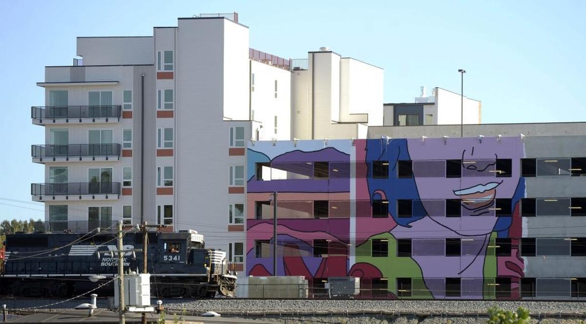 A train passes by part of a mural being installed on the side of the garage at the Novel NoDa apartment building. Crescent Communities’ installation of large artwork at Stonewall Station, may be the city’s largest outdoor artwork.