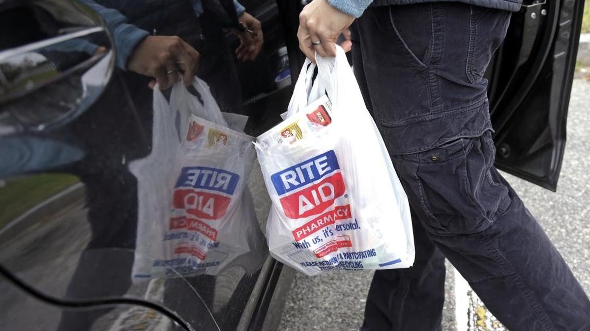In this file photo, a shopper carries her purchases from Rite Aid into her car, in North Andover, Mass. Walgreens and Rite Aid will sell 865 stores to rival retailer Fred’s for $950 million, possibly removing the final roadblock preventing the tie up between the nation’s largest and third-largest drugstore chains.