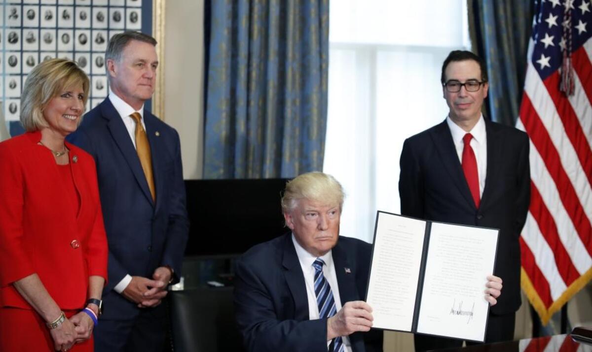 President Donald Trump, accompanied by, from left, Rep. Claudia Tenney, R-N.Y., Sen. David Perdue, R-Ga., and Treasury Secretary Steve Mnuchin, holds up a signed Executive Order, Friday, April 21, 2017, at the Treasury Department in Washington.