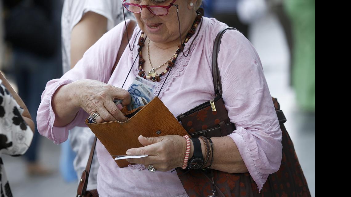 
A customer places her daily cash machine withdrawal limit of 60 euros into her purse after using an automated teller machines outside a closed Eurobank Ergasias bank branch in Athens. 
