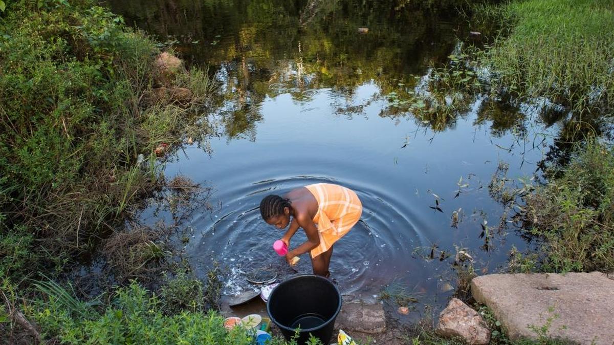 Osyanda Misidjan, 17, washes dishes on the banks of the Coermotibo River in her village of Adjuma Kondre, Suriname. Once surrounded by rainforest, the green palm trees and valley soccer field of the village are now surrounded by stony, bauxite-red plains left over from Alcoa’s mining operations that ceased in 2015.