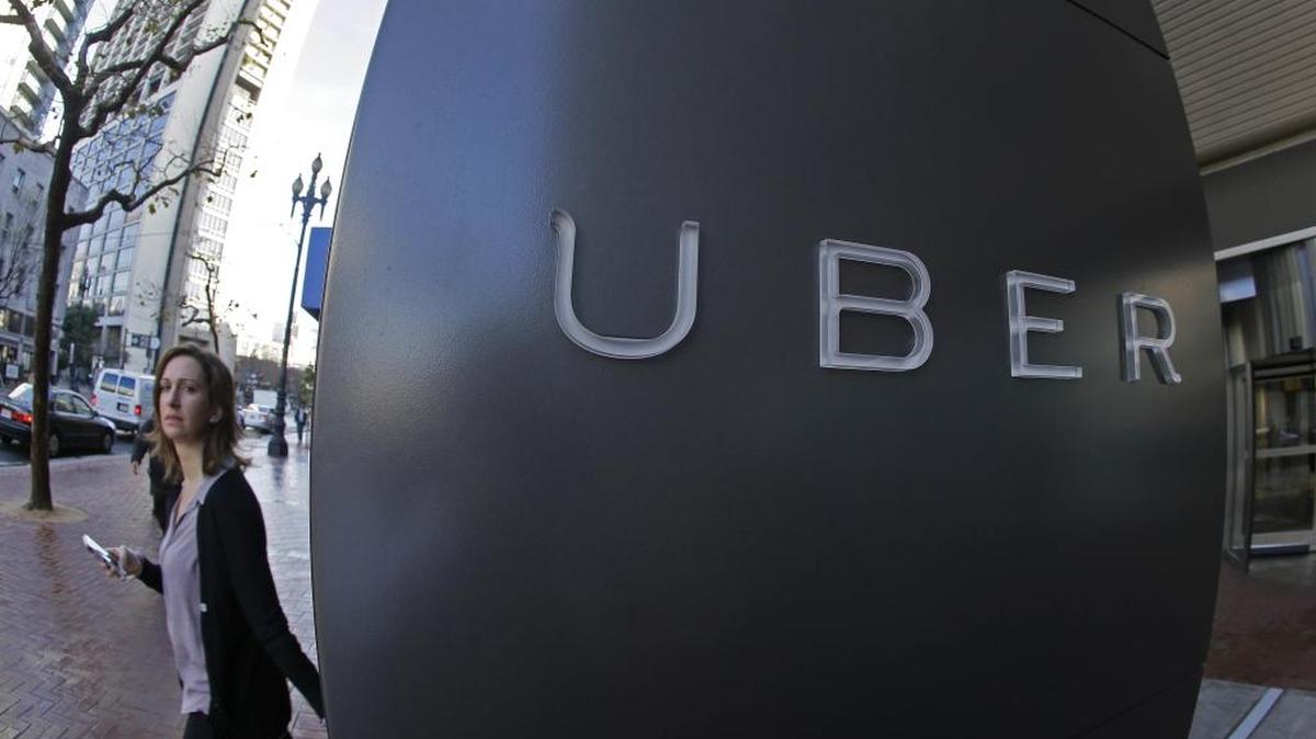 In this file photo , a woman walks past the company logo of the internet car service, Uber, in San Francisco.