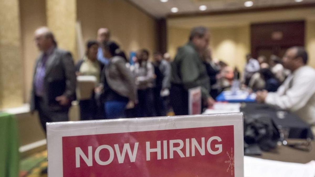A photo of a ‘now hiring’ sign at a career fair.