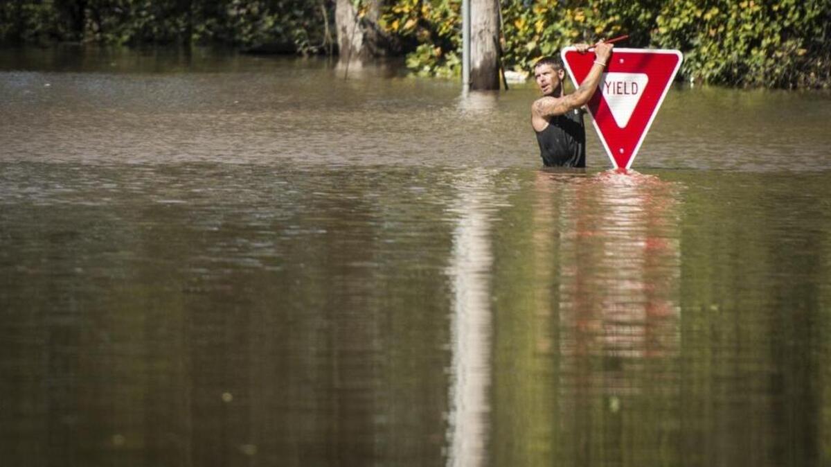 A man holds onto a yield sign after trying to swim out to help a stranded truck driver at NC 301 Highway and Tom Starling Road in Hope Mills (Cumberland County) on Sunday. Both people were rescued.