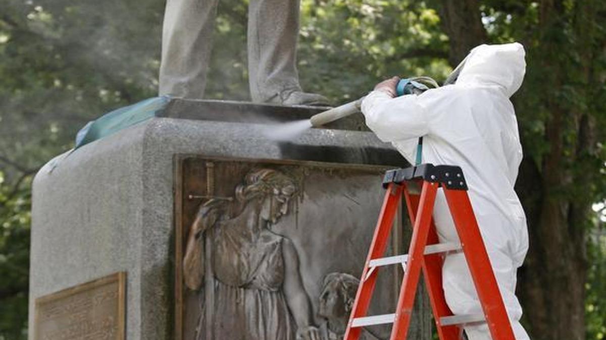 
A CCI Environmental Services worker holds the ladder for another worker as he blasts graffiti from the sandstone base of “Silent Sam” on the UNC Chapel Hill campus Tuesday. The spray of pulverized glass and water was expected to remove the black acrylic spray paint without harming the statue. 
