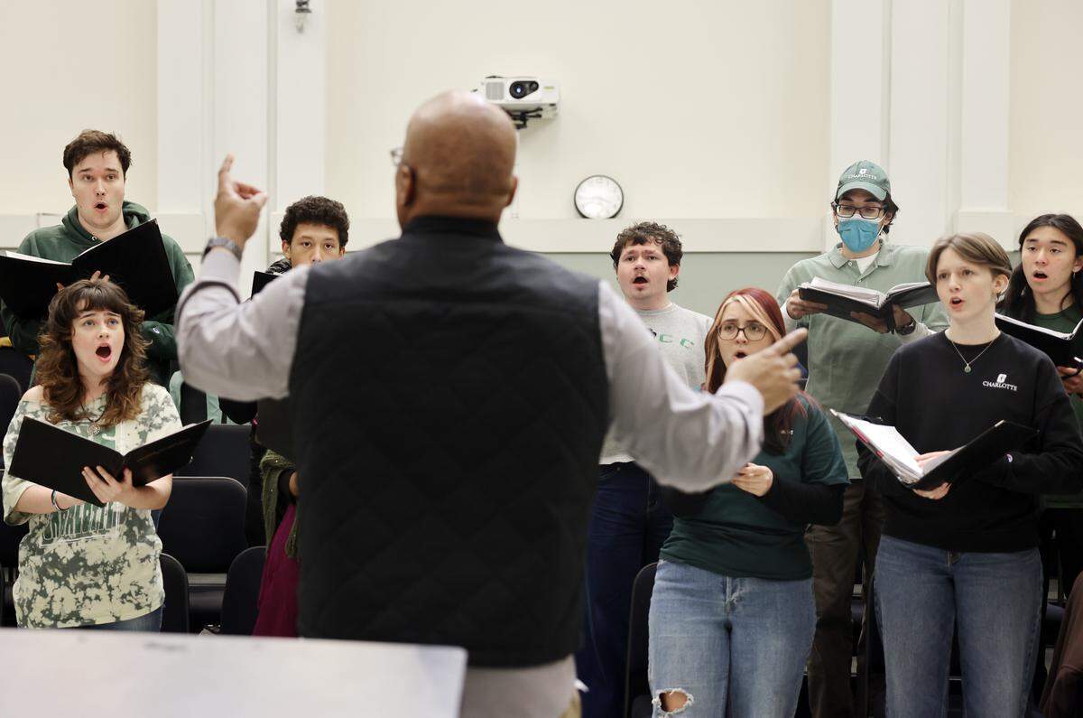 Jason Dungee, director of choral activities, leads a chorus at UNC Charlotte. They were rehearsing for an upcoming performance of songs related to the new book, “Partisan Song.”