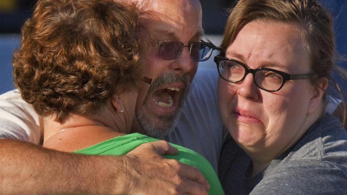 File - In this July 20, 2012 file photo, Tom Sullivan, center, embraces family members after losing his son Alex in the Aurora movie theater shooting, in Aurora, Colo. As the start the trial of the shooting spree defendant James Holmes approached, Sullivan told The Associated Press that, (before the shooting), “I didn’t know it was anything that I needed to worry about. But I was wrong,’’ he said. “Someone else’s son having a mental problem, having easy access to weapons, all of a sudden became my problem.’’ (AP Photo/Barry Gutierrez, file)