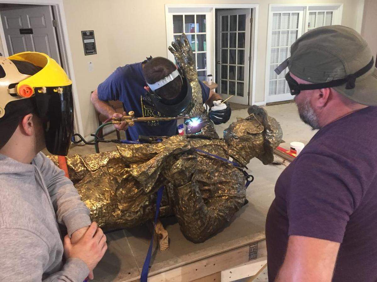 Case Baumgarten (left) and Christopher Morton (right) look on as Jason Stein works at repairing damage to the Hugh McManaway statue’s arm.