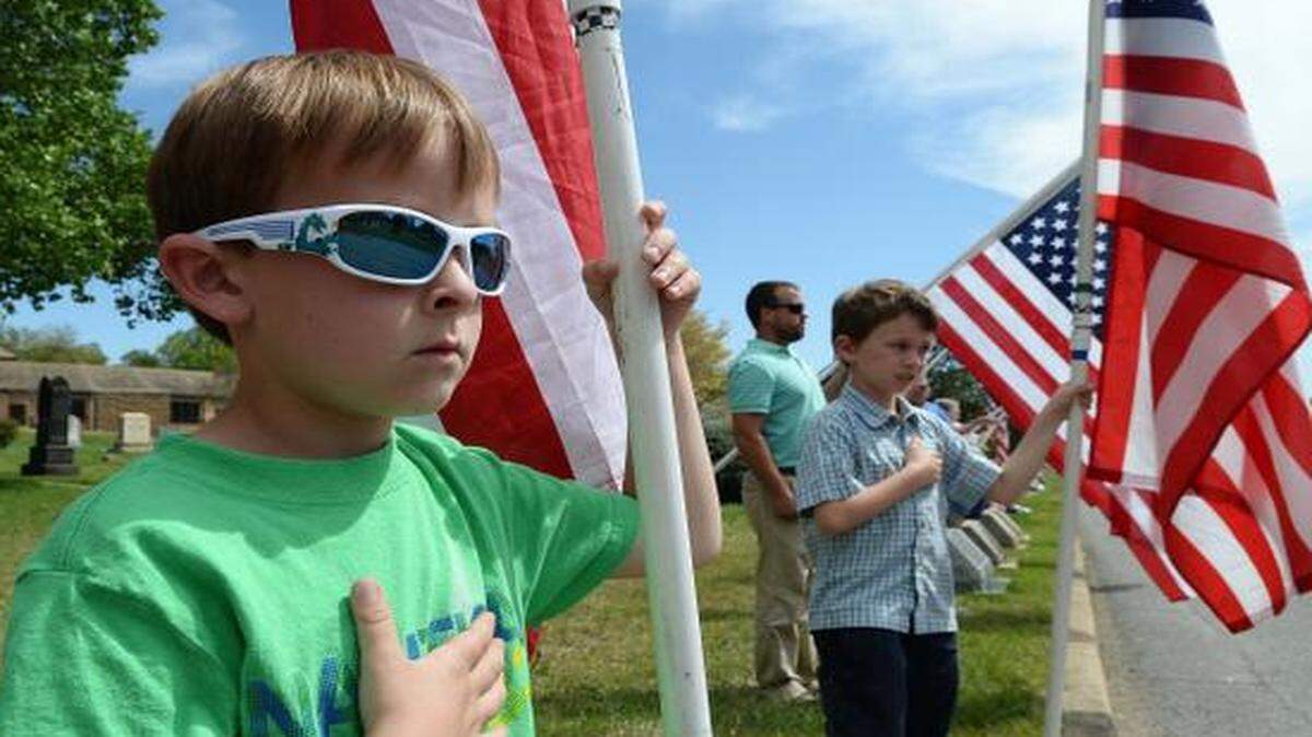 
 Liam Hinkle 6 (left), of York,SC a relative of Bunyan Price Jr., holds a flag in honor of Sgt. Price, Henry Eldridge 8 (right), of York,SC at the entrance to Greenwood Cemetery on S. Main street in Belmont for the funeral procession for Sgt. Bunyan Price Jr, a Belmont soldier killed in the Vietnam War, his casket was carried in a 1800s horse-drawn hearse into the Greenwood Cemetery in Belmont April 11,2015.
