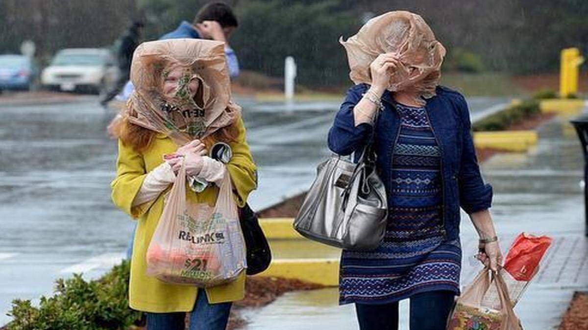 
Left to right sisters Rebecca and Kathleen Figmaup use grocery bags to shield themselves from the rain and wind at the Quail Corners Harris Teeter on March 5, 2015.
