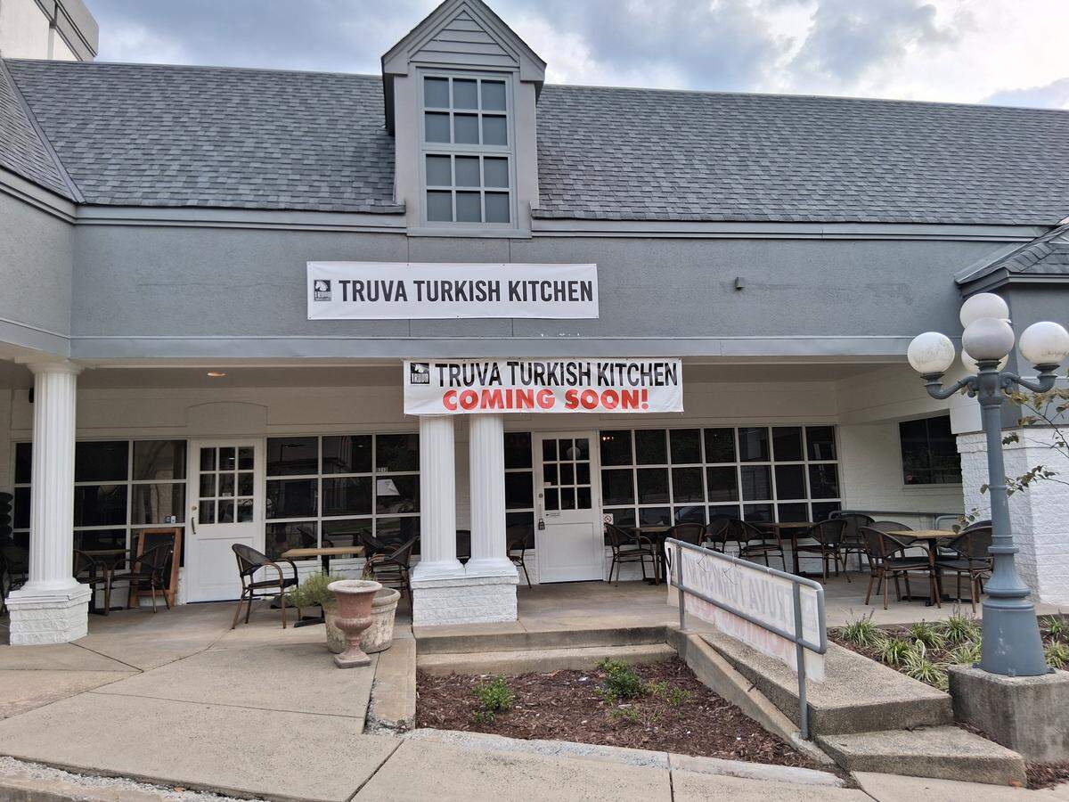 The exterior of a restaurant building, which has a gray roof and a white covered patio supported by columns. Two banners are visible; one above the patio reads TRUVA TURKISH KITCHEN, and a lower one announces TRUVA TURKISH KITCHEN COMING SOON!