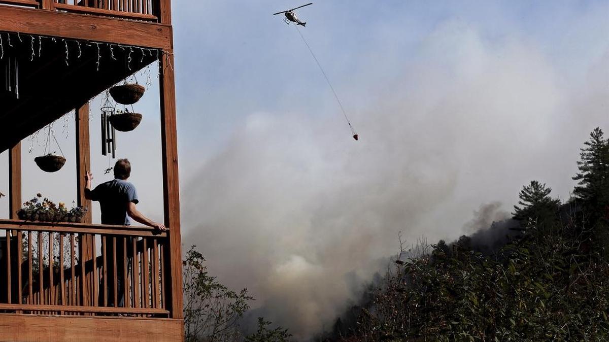 Eric Willey looks on from the porch of his home as a helicopter works on dropping water on the approaching Rock Mountain wildfire Wednesday n Tate City, Ga. Residents are under a pre-evacuation order as firefighters work to keep the fire away from their homes.