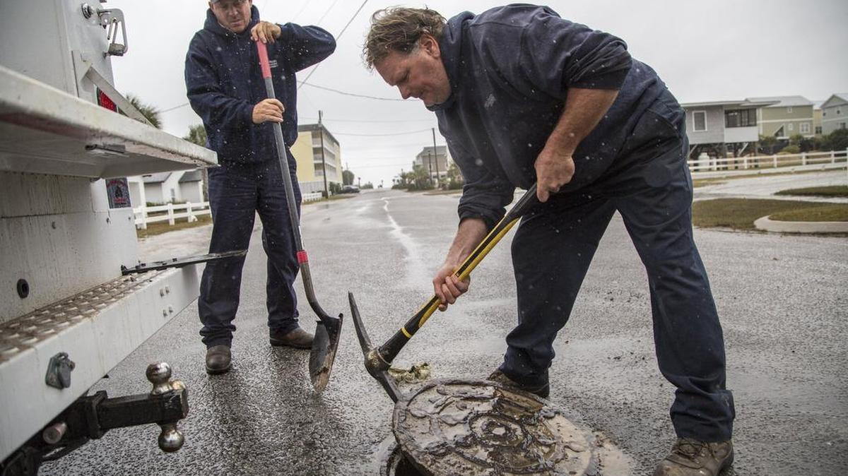 Craig Grainger (left) and Howie North with Grand Strand Water and Sewer Authority install in-flow protectors under man holes to keep the high tides from entering the sewer system.