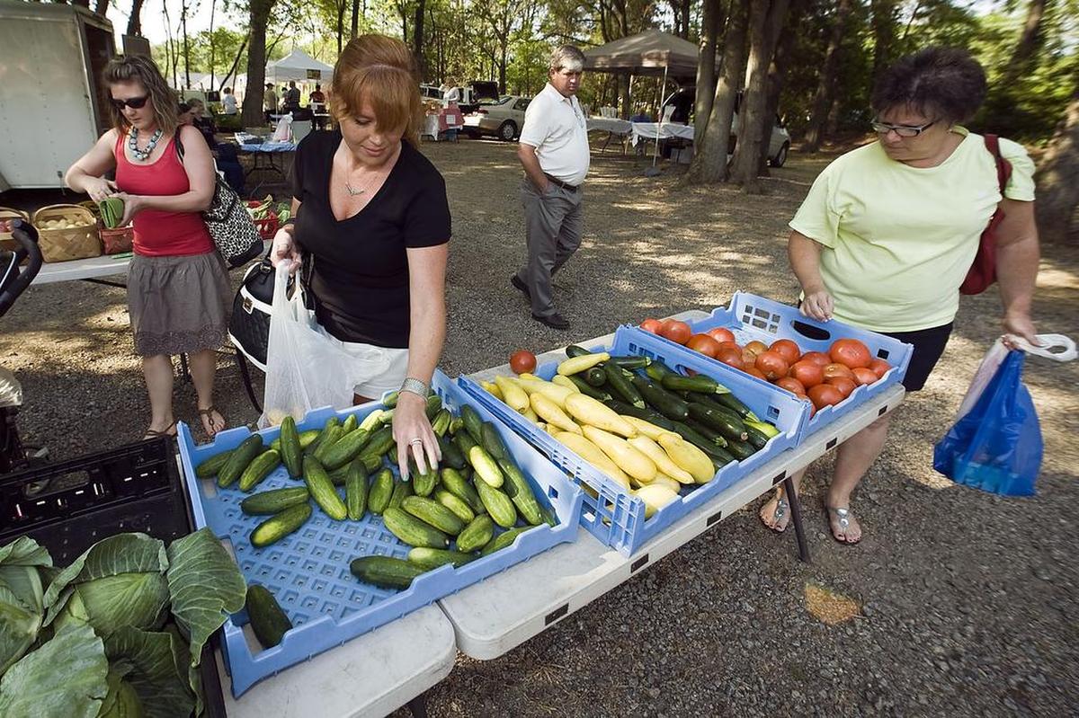 Charlotte resident Meridia Burris, left foreground, looks at the cucumbers as Harrisburg resident Carla Davis, right, selects a tomato at the Karriker’s Produce tables during The Harrisburg Market.
