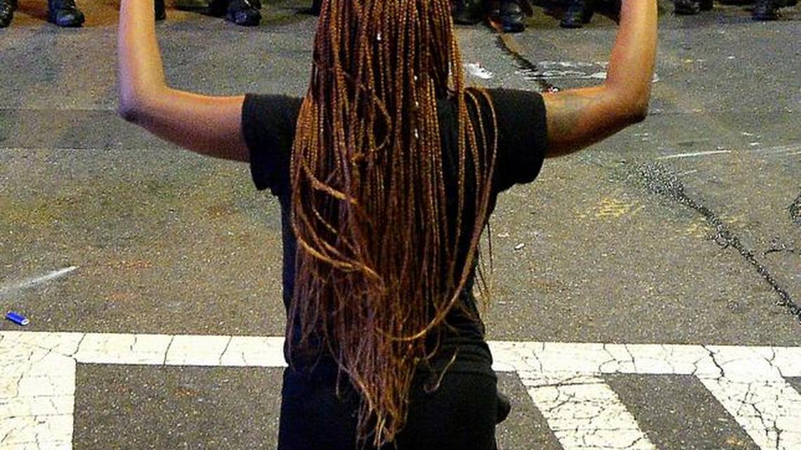 A protestor places her arms in the air while on her knees in front of CMPD officers in riot gear at the intersection near the Epicentre in Charlotte on Sept. 21, 2016. Protestors were marching and rallying against CMPD officer Brentley Vinson’s fatal shooting of Keith Lamont Scott on Tuesday evening at The Village at College Downs apartment complex in the University City area.