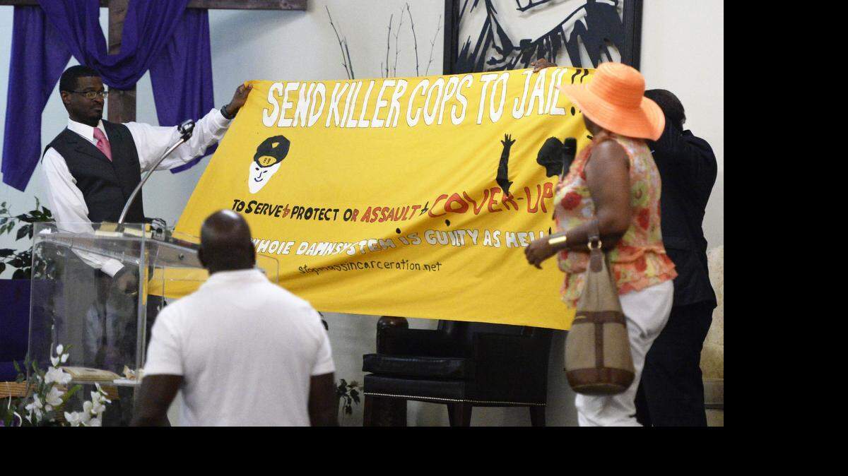 
John C. Barnett, left, of True Healing Under God (THUG) Civil Rights Organization helps to unveil a protest banner made by Deborah Phelps, right, of StopMassIncarceration.Net during a rally at Redemption Christian Ministries on Sunday, July 19, 2015, in advance of the trial of suspended Charlotte-Mecklenburg Police officer Randall Kerrick.
