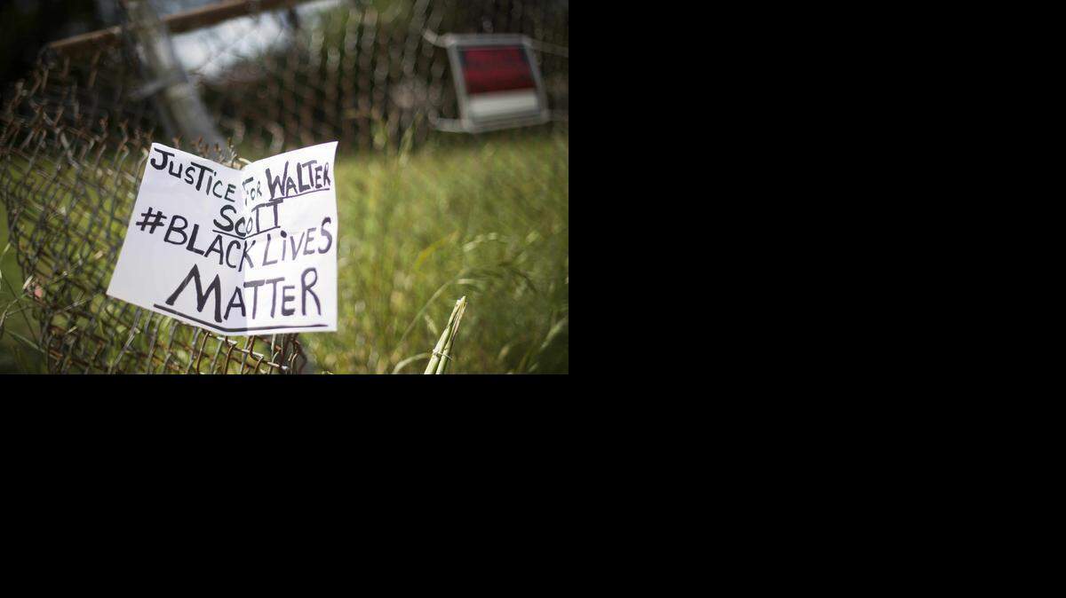 
TOPSHOTS A placard is tied to a fence outside the vacant lot where Walter Scott, the 50-year-old man who was fired at eight times was killed as he ran away from an officer after a traffic stop in North Charleston, South Carolina on April 8, 2015. Police officer Michael Slager,33, who fatally shot Scott in the US city of North Charleston has been fired after he was charged with murder, the mayor said. Speaking at a highly charged press conference frequently interrupted by residents angered at America's latest high-profile police killing of a black man, Mayor Keith Summey said the city had moved quickly to fire the officer after Saturday's shooting. AFP PHOTO/JIM WATSONJIM WATSON/AFP/Getty Images 
