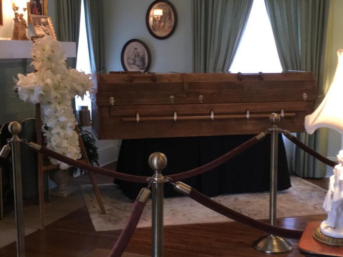 Graham’s wooden casket, with a cross nailed on the front, is on a black bier in what was once the living room of his family’s home on Park Road. A cross-shaped arrangement of lilies is on a stand next to the casket.