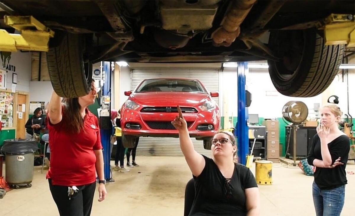 Myers Park High auto mechanics teacher Kristina Carlevatti (left) asks student Evelyn Harris to show her where the leak is under the car. Anna Payne, another student, watches.