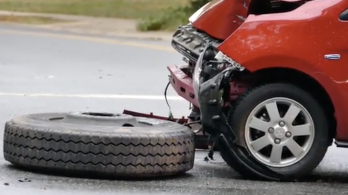 One of two rear wheels that detached from a CMS bus Tuesday morning rests near a damaged car on Eastway Drive.