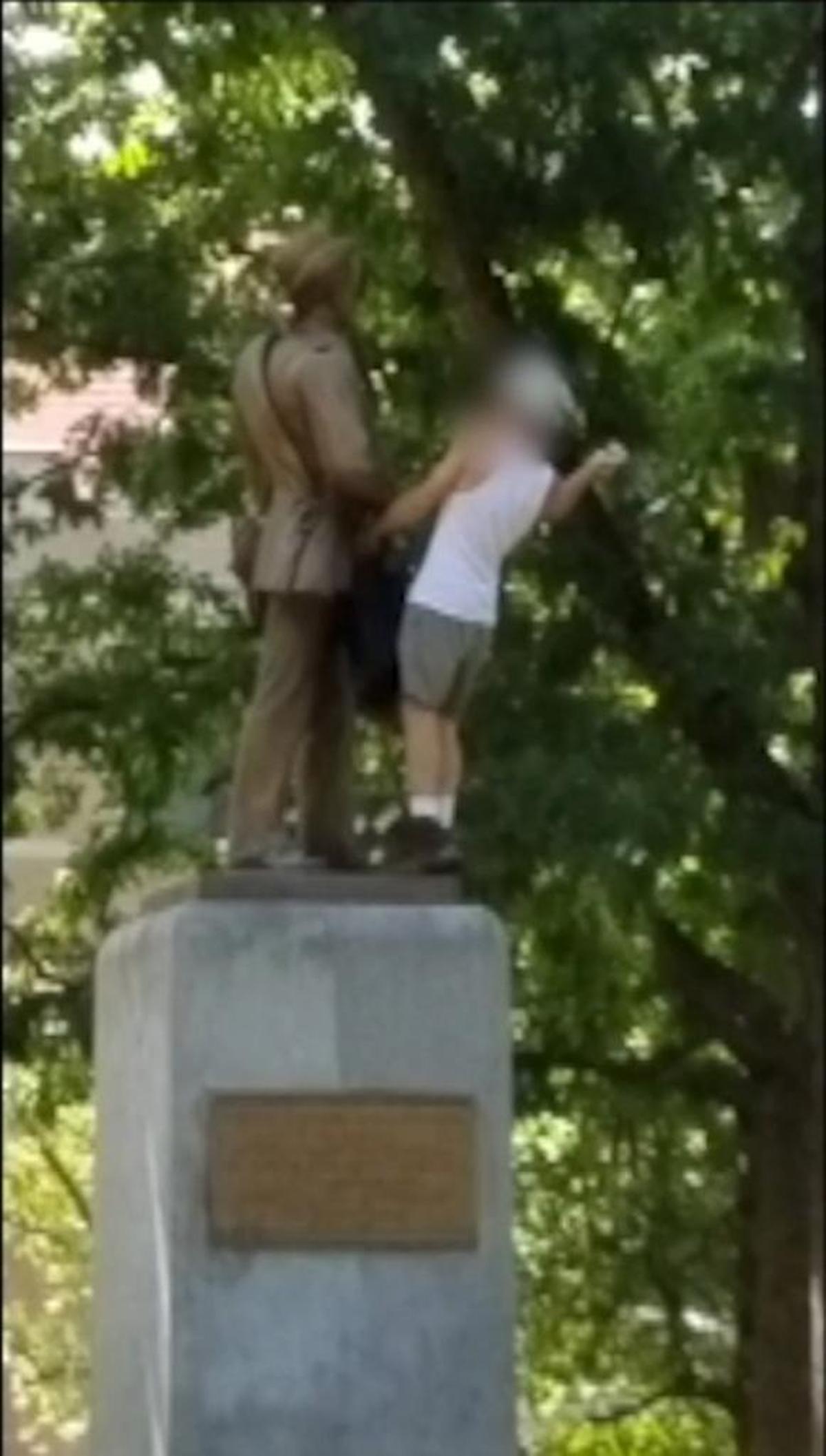 Still image from a video shows an unidentified man hammering the face of the Confederate Silent Sam statue on the UNC campus in Chapel Hill. The man's face was blurred by the videographer.