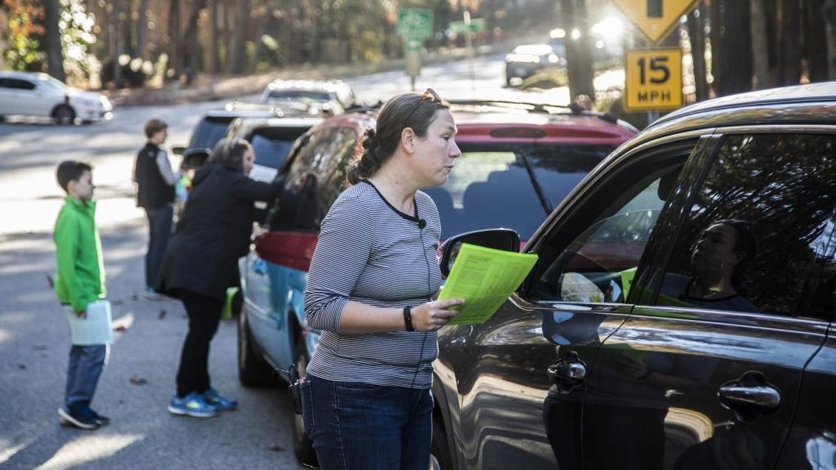 Ann Spencer of Combs Elementary School PTA in Raleigh talks with parents as they wait in carpool line Monday. Volunteers ae urging parents to ask state legislators to give school districts flexibility on the new K-3 class sizes going into effect in July.
