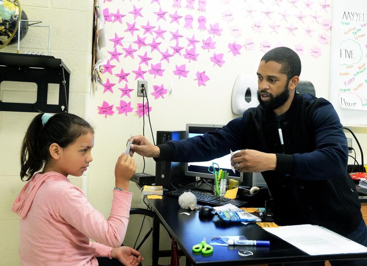 Science coach Marcus McKoy helps Savannah Stevey, 11, look through a device that replicates a cornea of the eye to see how the eye flips an image at a certain distance.