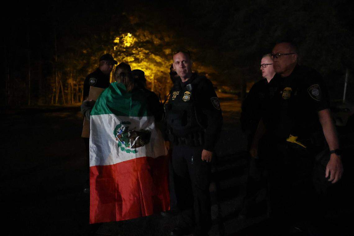A person donning a Mexican flag walks by federal police during a protest against Border Patrol outside the Department of Homeland Security/ICE headquarters on Tyvola Center Drive in Charlotte, NC on Sunday, November 16, 2025.