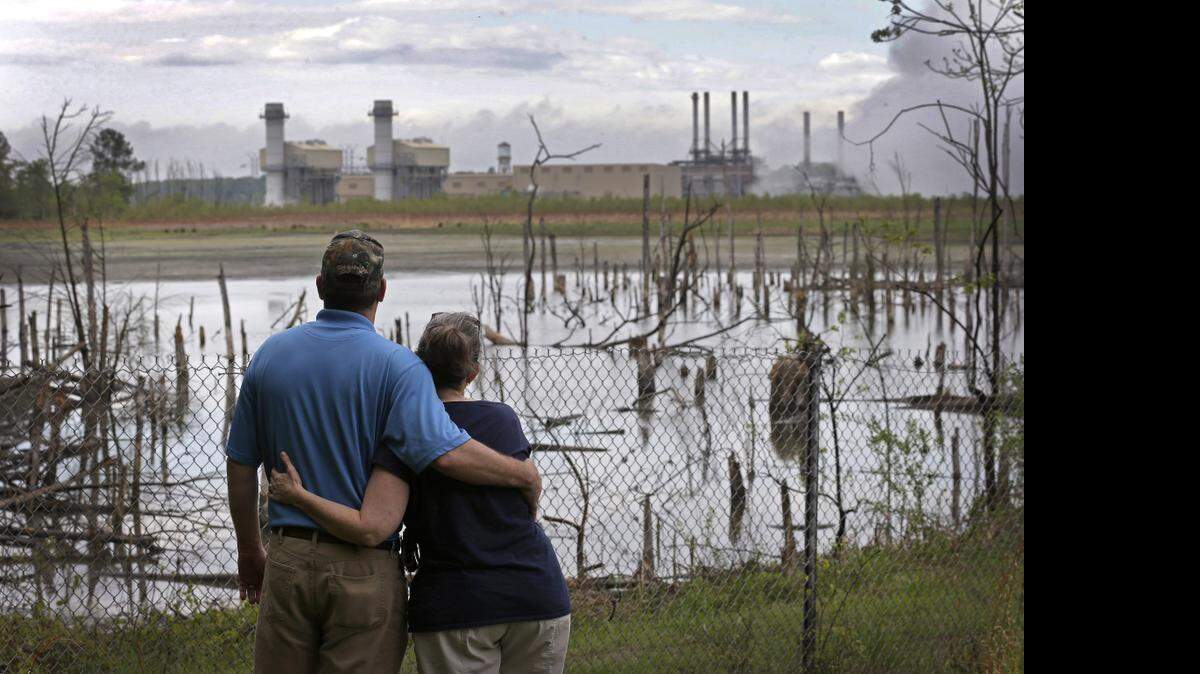 
 Bryant Gobble, left, hugs his wife, Sherry Gobble,  in April 2014 as they look from their yard across an ash pond full of dead trees toward Duke Energy’s Buck Steam Station in Dukeville.
