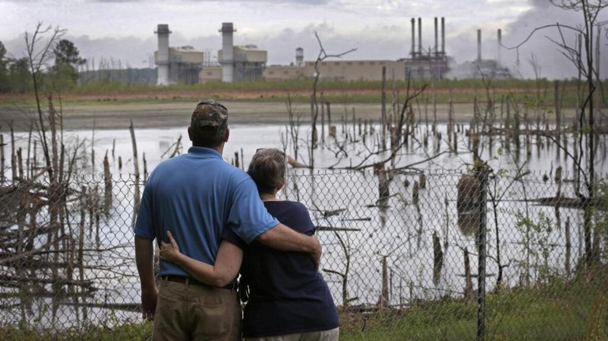 Bryant Gobble hugs his wife Sherry Gobble as they look from their yard across an ash pond toward Duke Energy's Buck Steam Station in Rowan County in this 2014 photo.