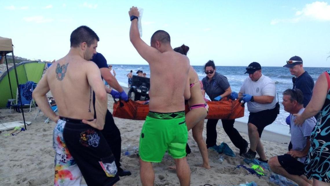 In this June 14, 2015 photo, emergency responders assist a teenage girl at the scene of a shark attack in Oak Island.