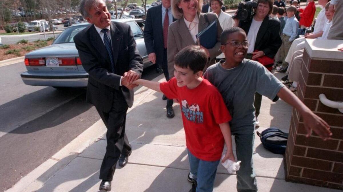In 1997, Elie Wiesel began a relationship with Charlotte when he made his first of three visits to the city, speaking to students and others and helping to birth the Echo Foundation. Here, he’s at Charlotte Lation with students and Stephanie Ansaldo, (holding binder) the president of the Echo Foundation.