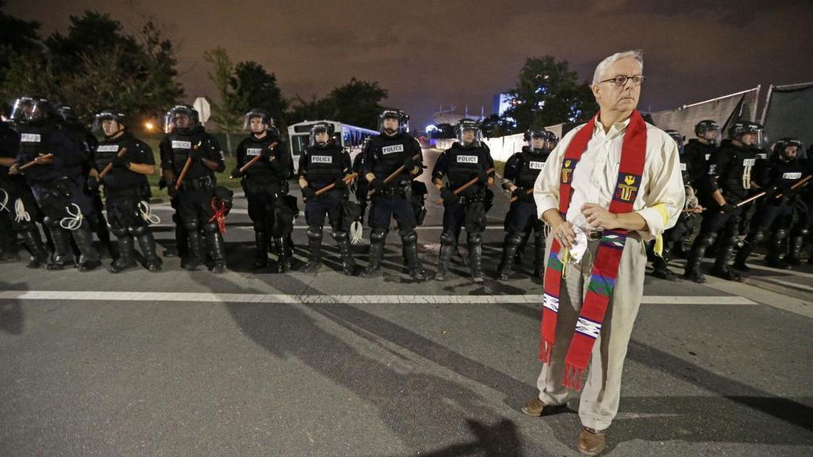 The Rev. John Cleghorn, Caldwell Presbyterian Church, stands in front of a line of police officers in Charlotte, N.C. Thursday, Sept. 22, 2016. blocking the access road to I-277 on the third night of protests following Tuesday's fatal police shooting of Keith Lamont Scott. (AP Photo/Chuck Burton)