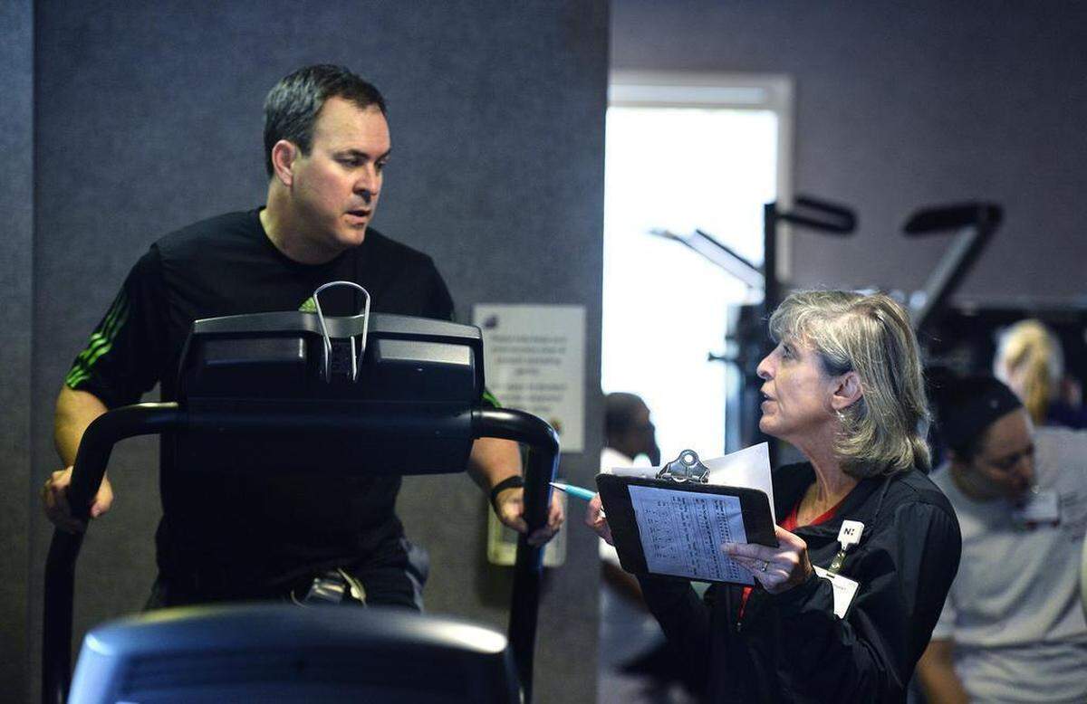 Nathan Taylor works out on an elliptical machine while Elaine Barnes monitors his vital signs.