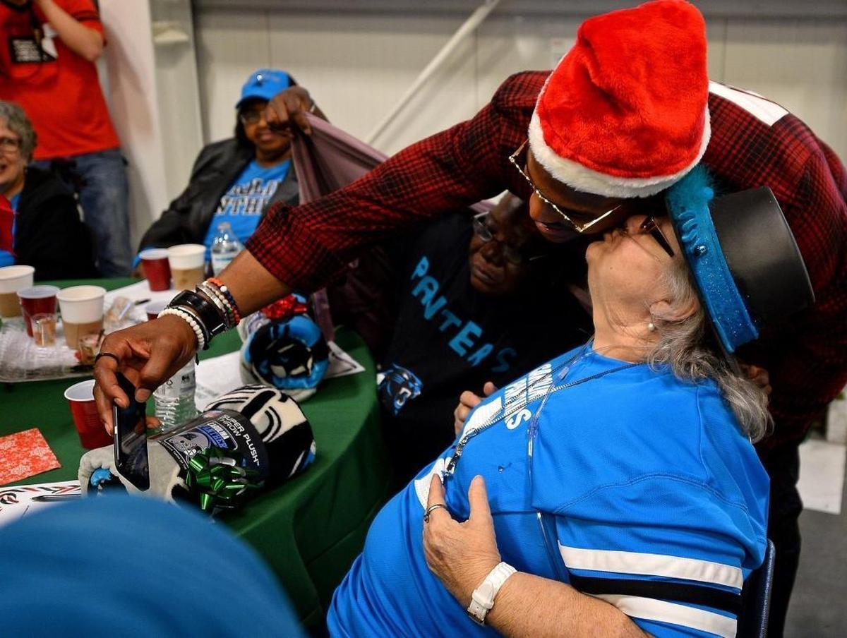 Barbara Benfield kisses Carolina Panthers quarterback Cam Newton on the cheek as he leans down to take a photograph with her during his Santa Cam’s Surprise Sleigh annual event. Newton and his helpers stopped at Second Harvest Food Bank to donate $25,000 to its “Second Helping” program and Panthers fleece blankets to 200 homebound seniors.